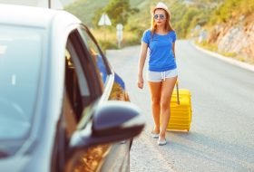 Young woman with a yellow suitcase goes to a car